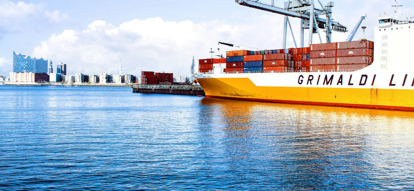 Orange-weißes Containerschiff im Hamburger Hafen, im Hintergrund die Elbphilharmonie